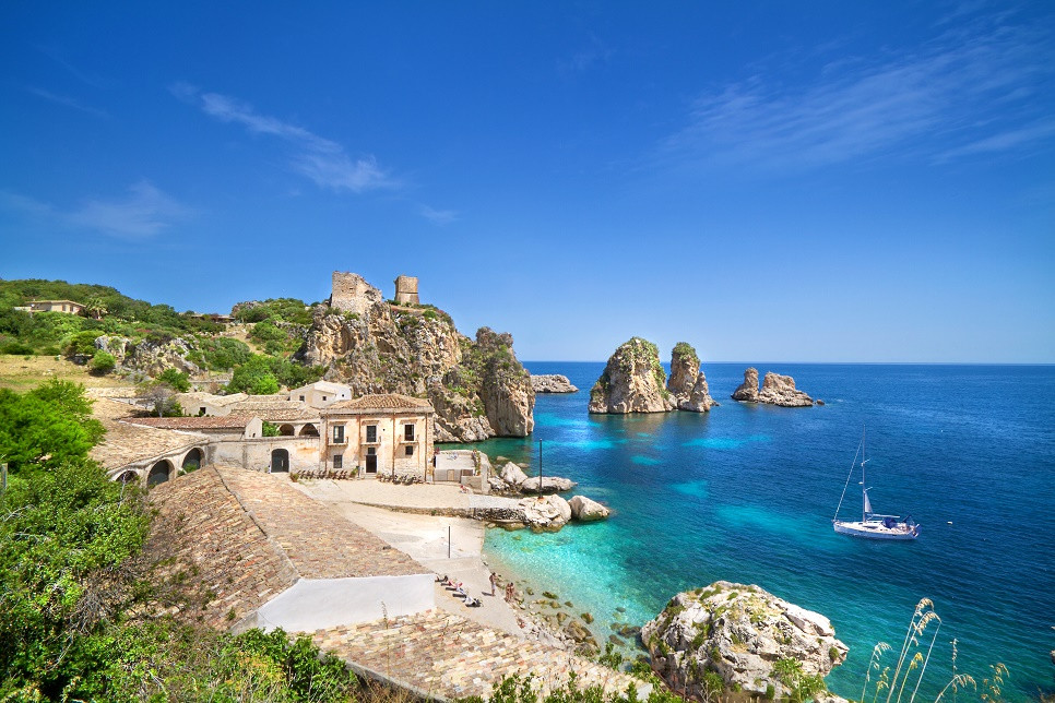 The historic Tonnara di Scopello and its sea stacks above clear blue water